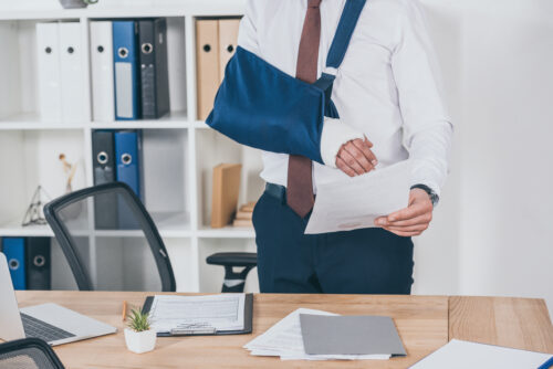 worker in office with broken arm in sling holding paper