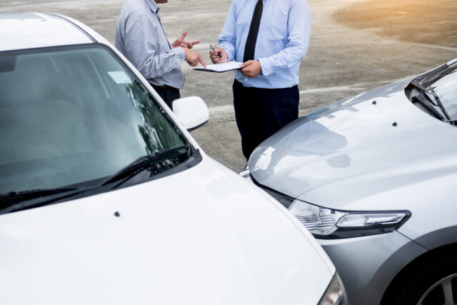 Insurance agent writing on clipboard while examining car after accident claim being assessed and processed