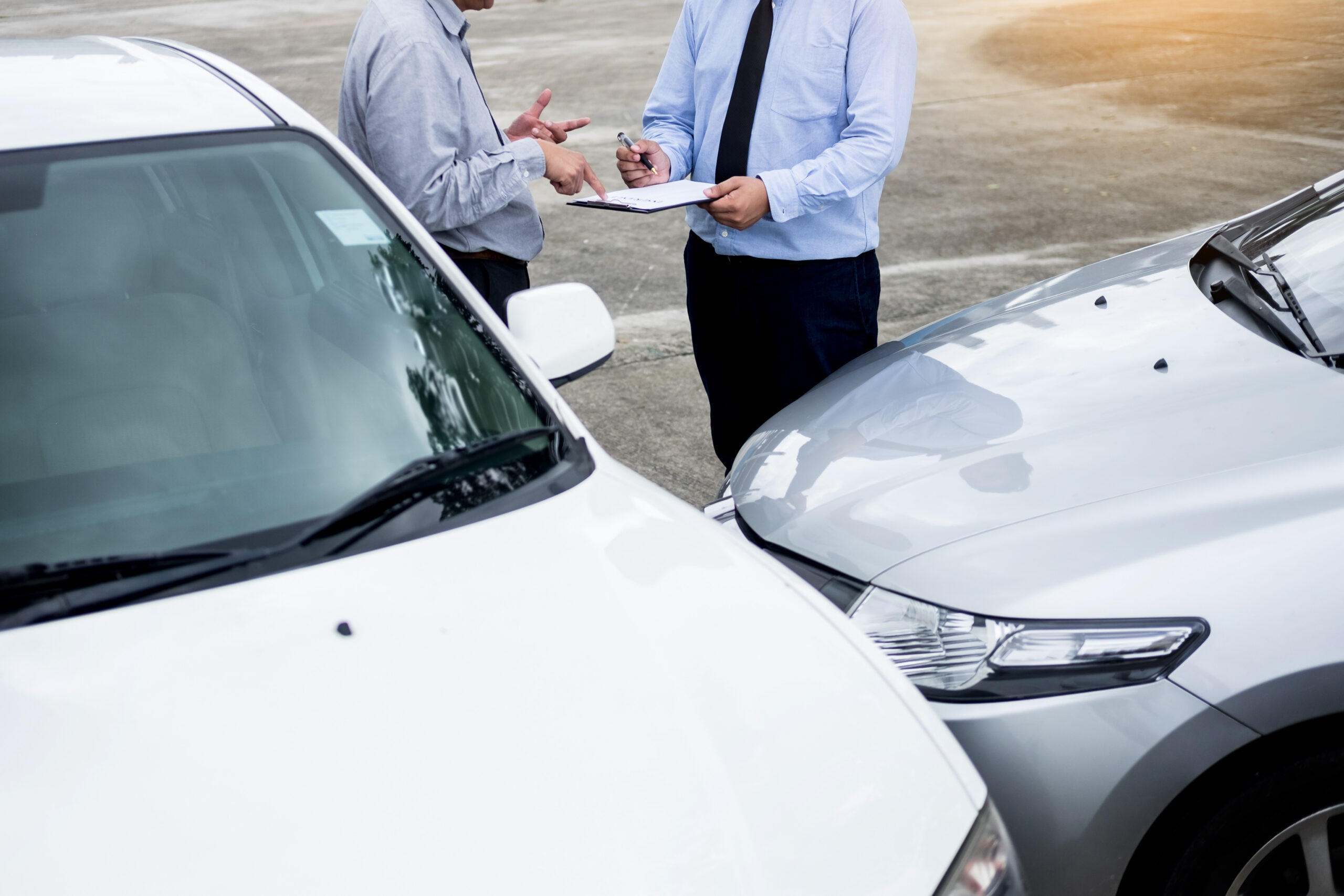Insurance agent writing on clipboard while examining car after accident claim being assessed and processed